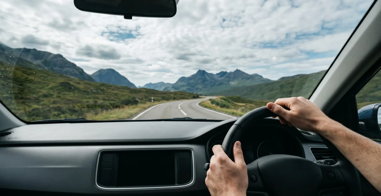 Driver enjoying scenic mountain road through windshield with winding highway ahead and dramatic landscape under expansive sky