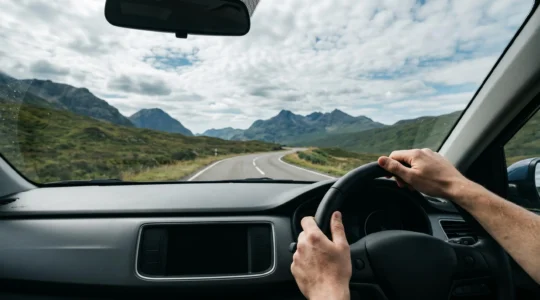 Driver enjoying scenic mountain road through windshield with winding highway ahead and dramatic landscape under expansive sky