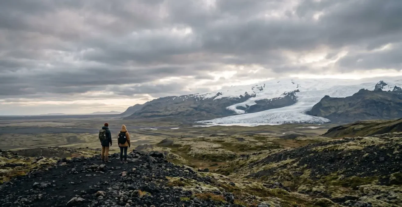 Two travelers exploring Iceland's dramatic volcanic landscape under atmospheric sky on budget adventure