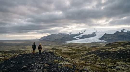Two travelers exploring Iceland's dramatic volcanic landscape under atmospheric sky on budget adventure