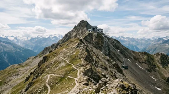 Expansive mountain panorama with dramatic elevation showing hiking trail and cable car infrastructure from aerial perspective