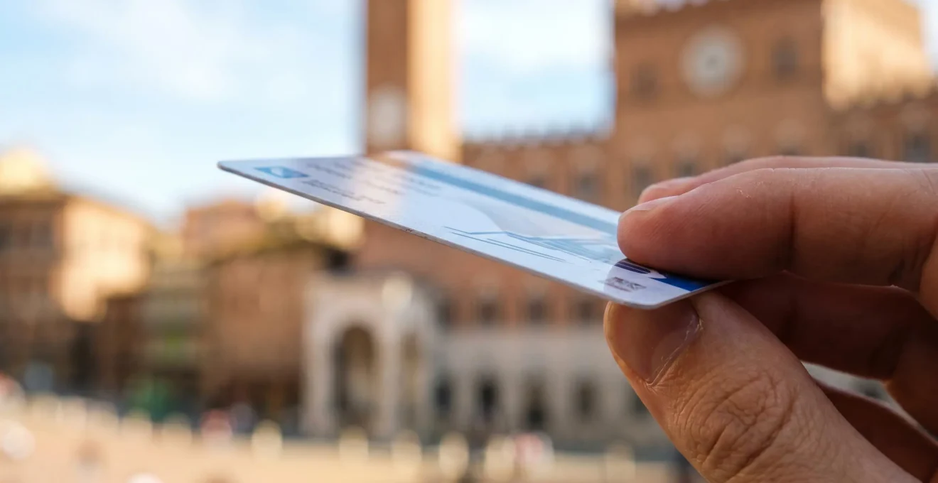 Extreme close-up of a multi-day bus pass card held in hand with a blurred Tuscan architectural landmark in soft bokeh background